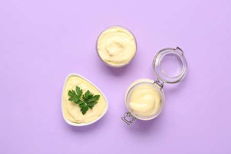 Bowls and jar of fresh mayonnaise on lilac backgroundの写真素材