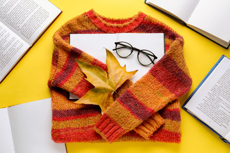 Composition with warm sweater, eyeglasses and books on yellow backgroundの写真素材