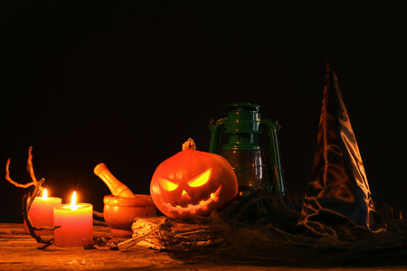 Halloween composition with jack-o-lantern, witch hat and burning candles on wooden tableの写真素材