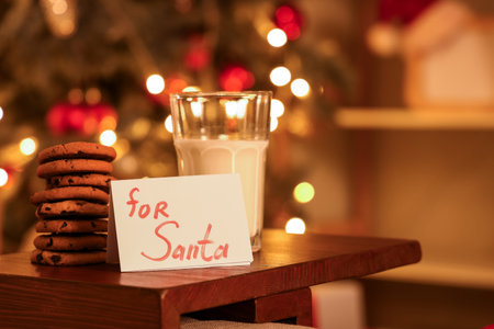 Paper with text FOR SANTA, Christmas cookies and glass of milk on table in room at night, closeupの写真素材