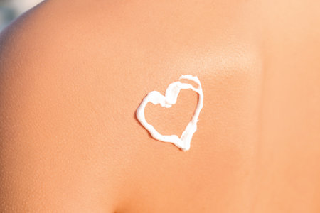 Heart drawn with sunscreen cream on young woman's back at sea resortの写真素材