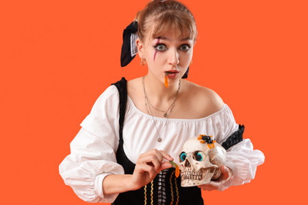 Young woman dressed for Halloween with skull and jelly candies on orange backgroundの写真素材
