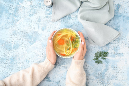 Woman eating tasty chicken soup on blue backgroundの写真素材