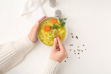 Woman adding dill into bowl with tasty chicken soup on whiteの写真素材