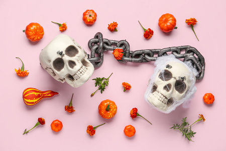 Human skulls with marigold flowers, pumpkins and chain on pink backgroundの写真素材