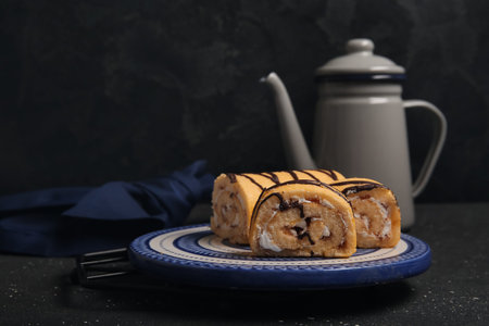 Plate with sweet sponge cake roll and cut pieces on black background