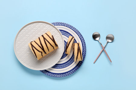 Plates with sweet sponge cake roll on blue background