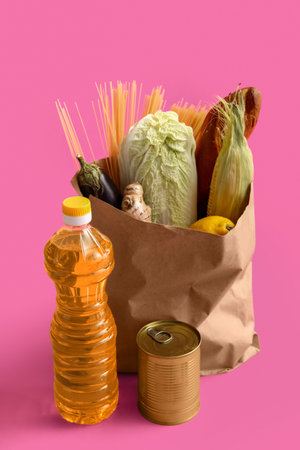 Paper bag with food products and bottle of oil on pink background