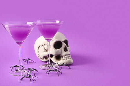 Glasses of delicious cocktail with skull and spiders for Halloween celebration on purple backgroundの写真素材