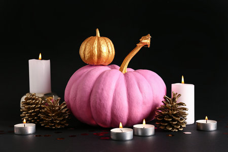 Painted pumpkins with golden cones and burning candles on black backgroundの写真素材