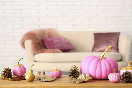 Pink painted pumpkins with autumn leaves and cones on wooden table near white brick wallの写真素材