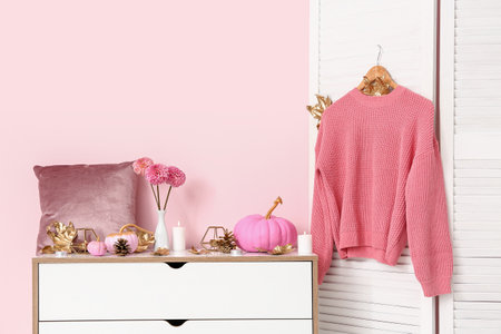 Painted pumpkins with autumn leaves and burning candles on chest of drawers near pink wallの写真素材