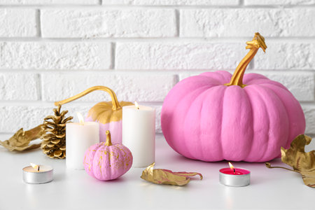 Painted pumpkins with autumn leaves and burning candles on table near white brick wallの写真素材