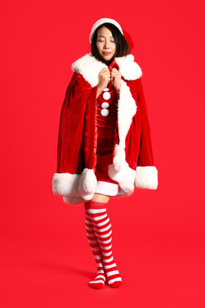 Young Asian woman in Santa costume on red backgroundの写真素材