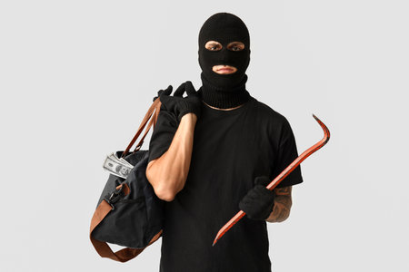 Male thief with crowbar and bag of money on gray backgroundの写真素材