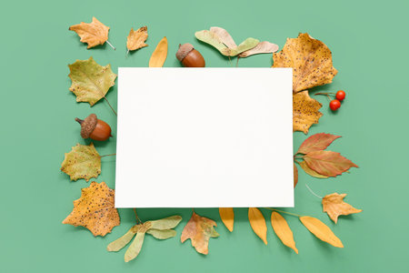 Autumn leaves with acorns and blank card on green background