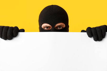 Male thief with blank poster on yellow backgroundの写真素材