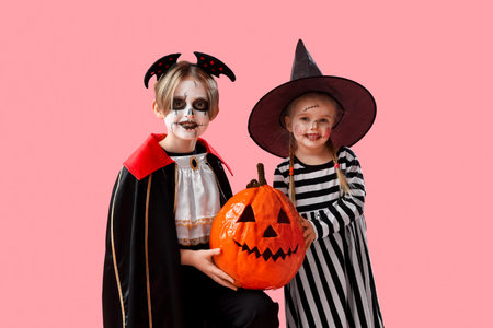 Little children dressed for Halloween with pumpkin on pink backgroundの写真素材