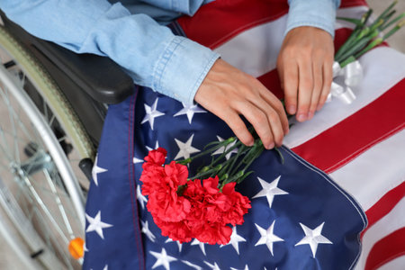 Young man with flowers and USA flag in wheelchair at home, closeup. Veterans Day celebrationの写真素材