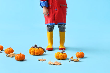 Little boy in rubber boots with pumpkins and autumn leaves on blue backgroundの写真素材