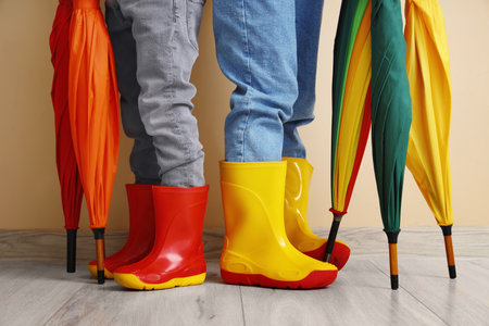 Little children in rubber boots with umbrellas near beige wall, closeupの写真素材