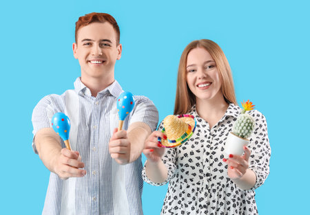 Young couple with Mexican maracas, sombrero hat and cactus on blue background