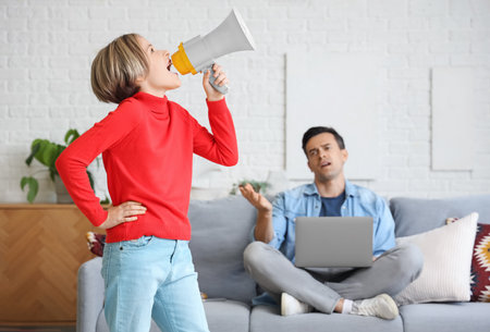 Noisy little boy shouting into megaphone and his stressed father at homeの写真素材