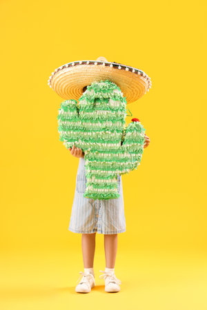 Little girl in sombrero hat with Mexican pinata on yellow backgroundの写真素材