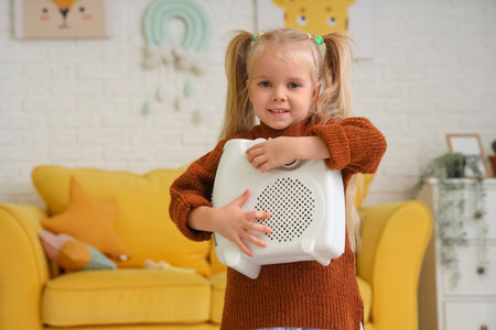 Cute little girl with electric heater at homeの写真素材