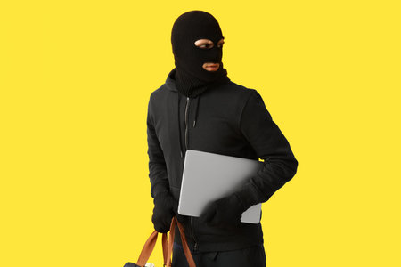 Male thief with laptop on yellow backgroundの写真素材