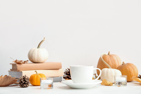 Cup of tea, books, autumn leaves, burning candles and pumpkins on white backgroundの写真素材