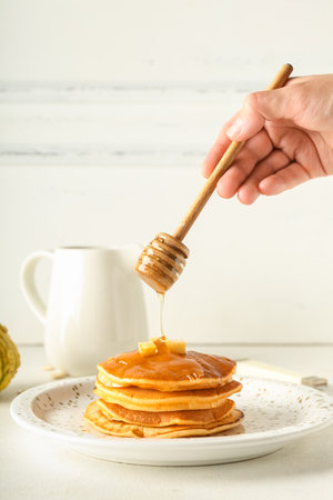 Woman pouring sweet honey onto tasty pumpkin pancakes on white backgroundの写真素材