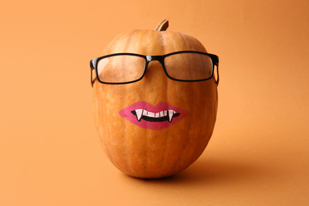 Halloween pumpkin with drawn lips, fangs and eyeglasses on orange backgroundの写真素材