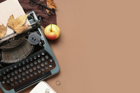 Vintage typewriter, apple, scarf, rings, eyeglasses and autumn leaves on brown backgroundの写真素材