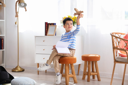 Cute little boy with adventure book and wooden airplane at homeの写真素材