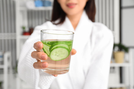 Young Asian woman with glass of cucumber water at home, closeupの写真素材