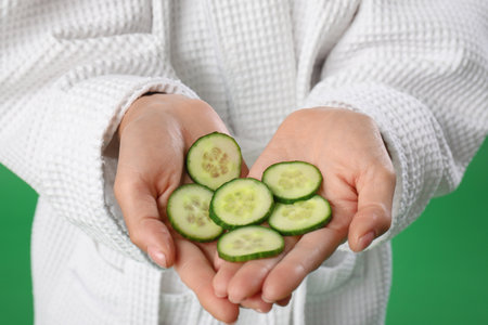 Young woman with cucumber slices on green background, closeupの写真素材