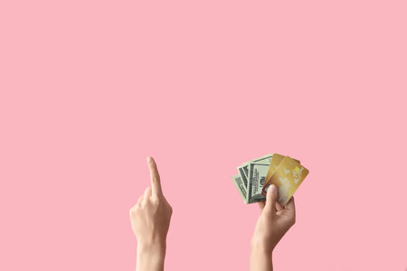 Woman with credit cards and cash pointing at something on pink backgroundの写真素材