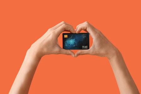 Woman with credit card making heart gesture on orange backgroundの写真素材