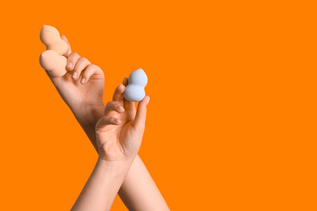 Female hands with different makeup sponges on orange backgroundの写真素材