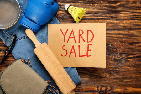 Cardboard with text YARD SALE and unwanted stuff on brown wooden background