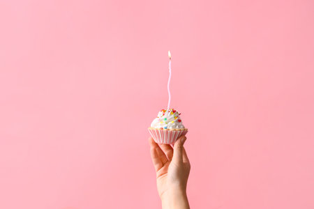 Woman holding tasty birthday cake with burning candle on pink backgroundの写真素材