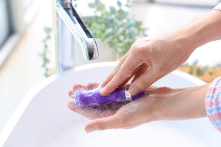 Woman washing vibrator over sink in bathroom, closeupの写真素材