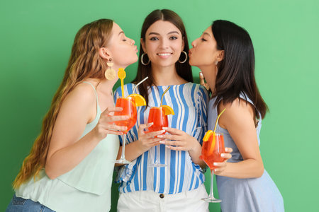 Beautiful young women with glasses of tasty spritz cocktail on green backgroundの写真素材