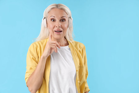Thoughtful mature woman in headphones on blue background