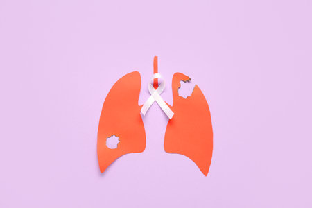Paper lungs with burnt holes and white ribbon on lilac background. Lung cancer conceptの写真素材