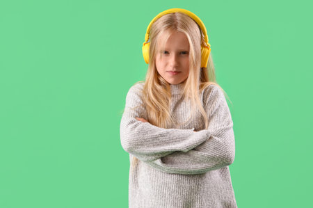 Upset little girl in headphones on green backgroundの写真素材