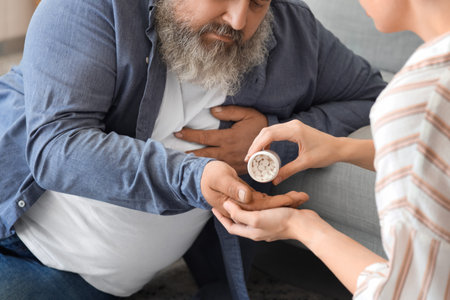 Young woman giving medicine to her father who is having heart attack at homeの写真素材