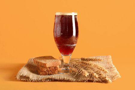 Glass of tasty kvass, bread and spikelets on orange backgroundの写真素材