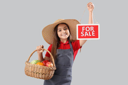 Little farmer with fresh food and FOR SALE sign on light backgroundの写真素材